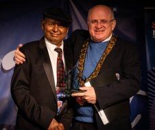 Two men in suits and ties are standing next to each other holding a trophy.