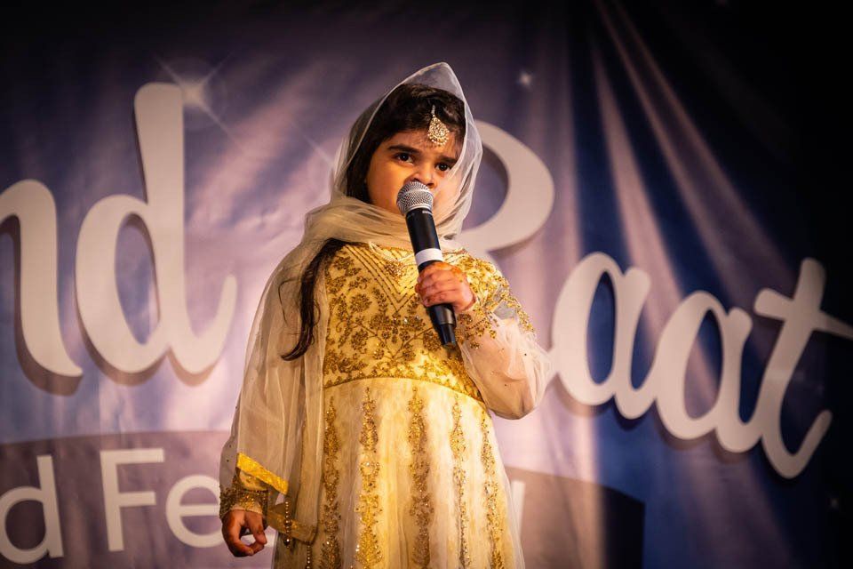 A little girl in a gold dress is singing into a microphone.