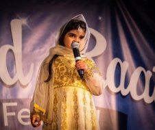 A little girl in a gold dress is singing into a microphone.