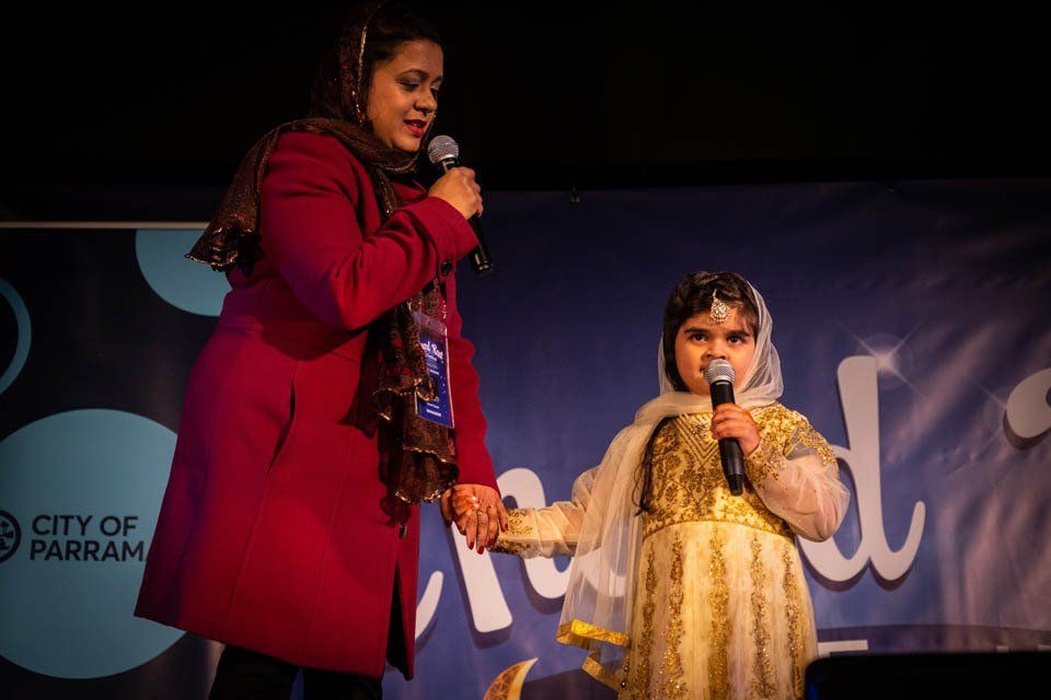 A woman is standing next to a little girl holding a microphone.