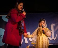 A woman is standing next to a little girl holding a microphone.