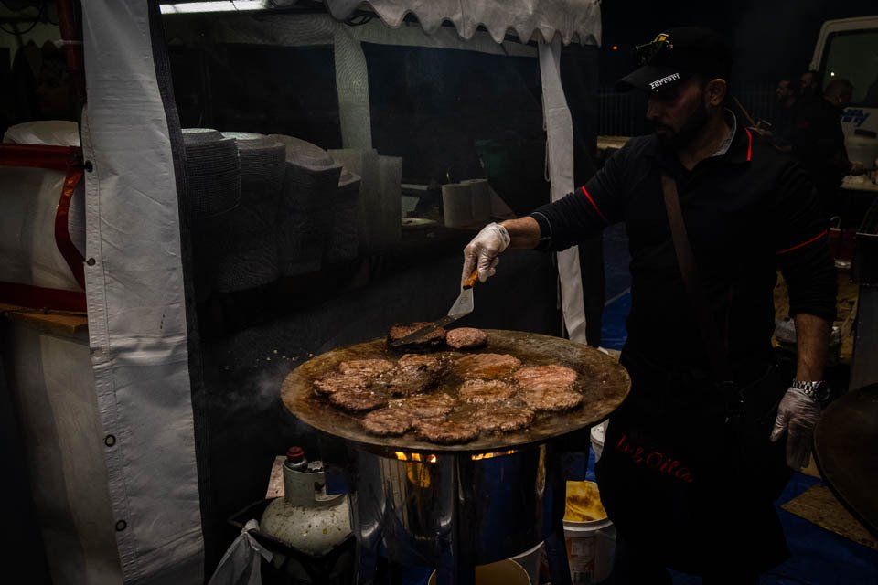 A man is cooking hamburger patties on a grill.