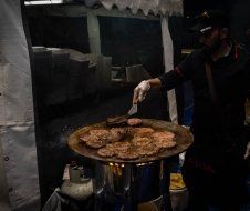 A man is cooking hamburger patties on a grill.