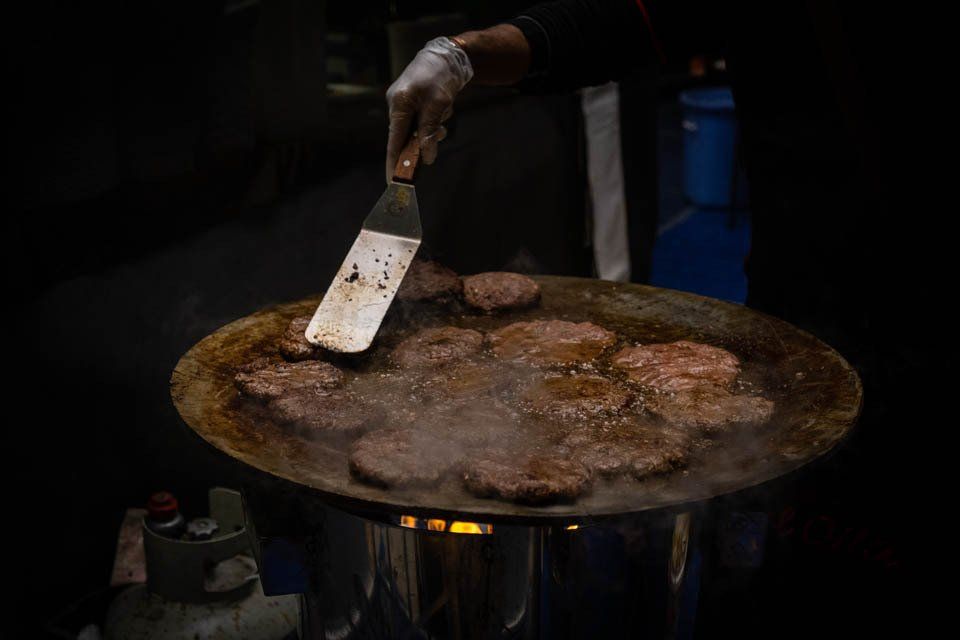 A person is cooking hamburger patties on a pan with a spatula.