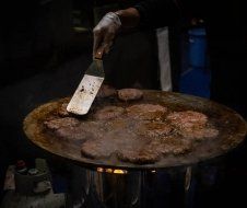 A person is cooking hamburger patties on a pan with a spatula.