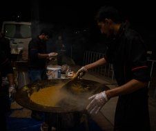 A man is cooking food in a large pan at night.