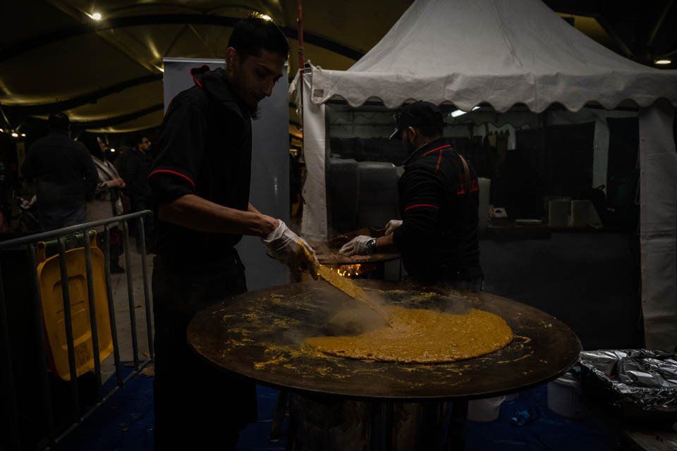 A man is cooking food on a large pan in front of a tent.