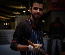 A man in an apron is holding two sausages in his hands.