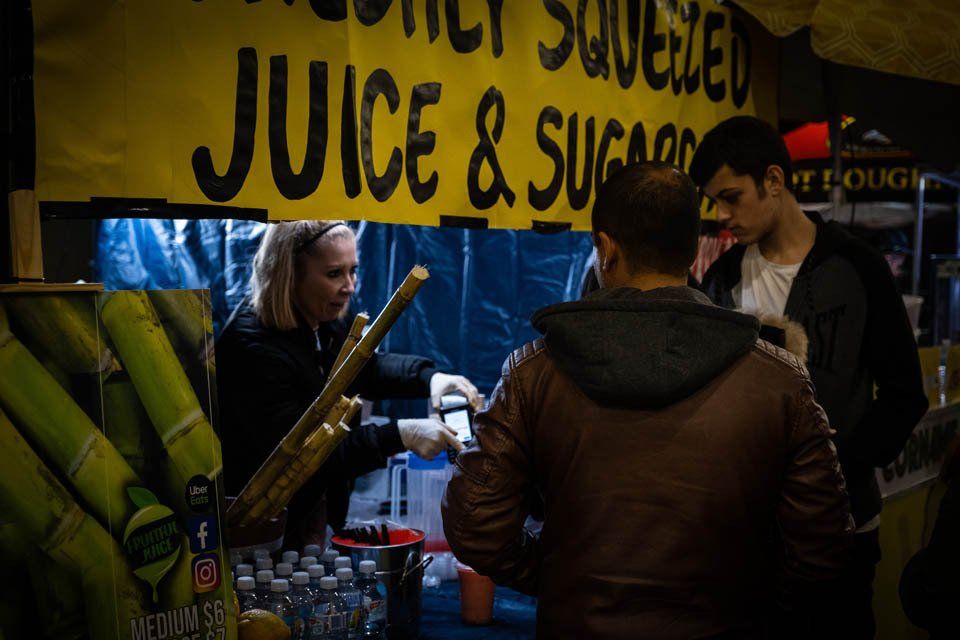 A group of people are standing around a juice and sugar stand.