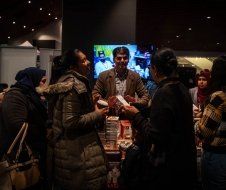 A group of people are standing around a table in a dark room talking to each other.