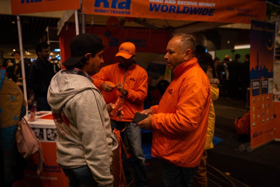 A man in an orange jacket is talking to a man in a gray hoodie.
