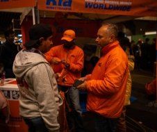 A man in an orange jacket is talking to another man