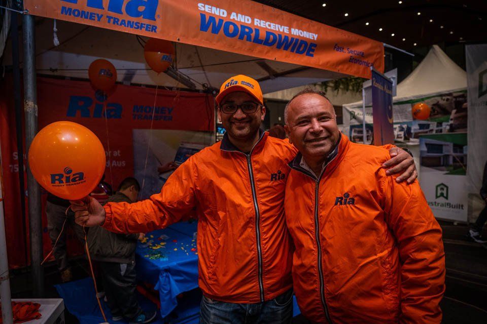 Two men are posing for a picture in front of a sign that says send and receive money worldwide.