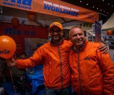 Two men are posing for a picture in front of a sign that says send and receive money worldwide.