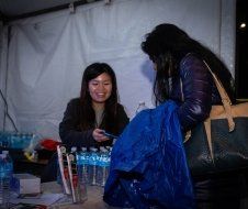 Two women are sitting at a table with bottles of water and a blue bag.