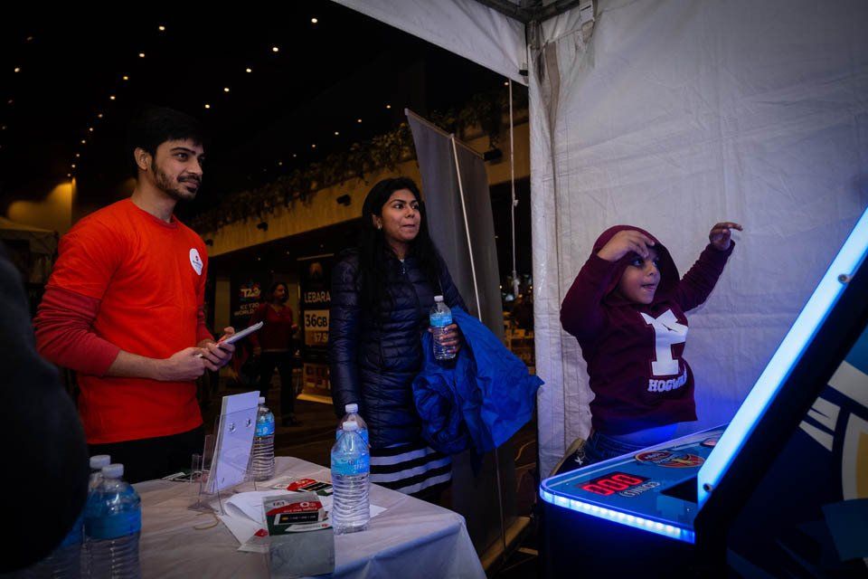 A man in a red shirt is standing next to a table with a child playing a video game.