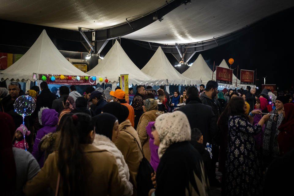 A crowd of people are gathered under tents at a festival.