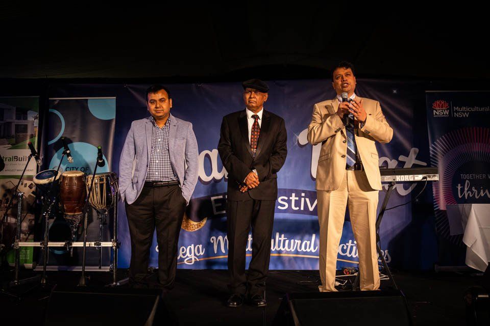 Three men in suits are standing on a stage holding microphones.