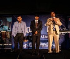 Three men in suits are standing on a stage holding microphones.