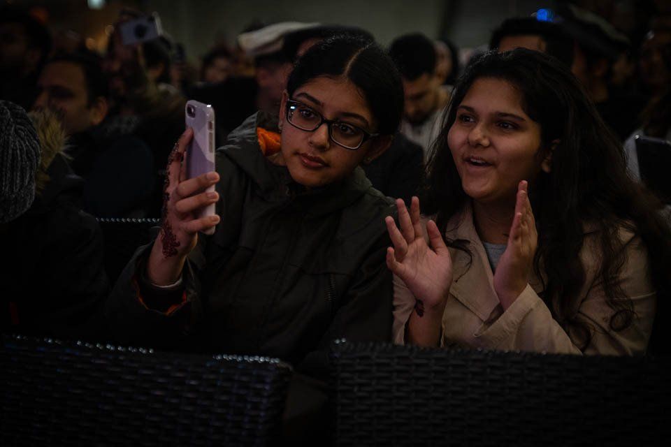 Two women are sitting in a crowd looking at a cell phone.