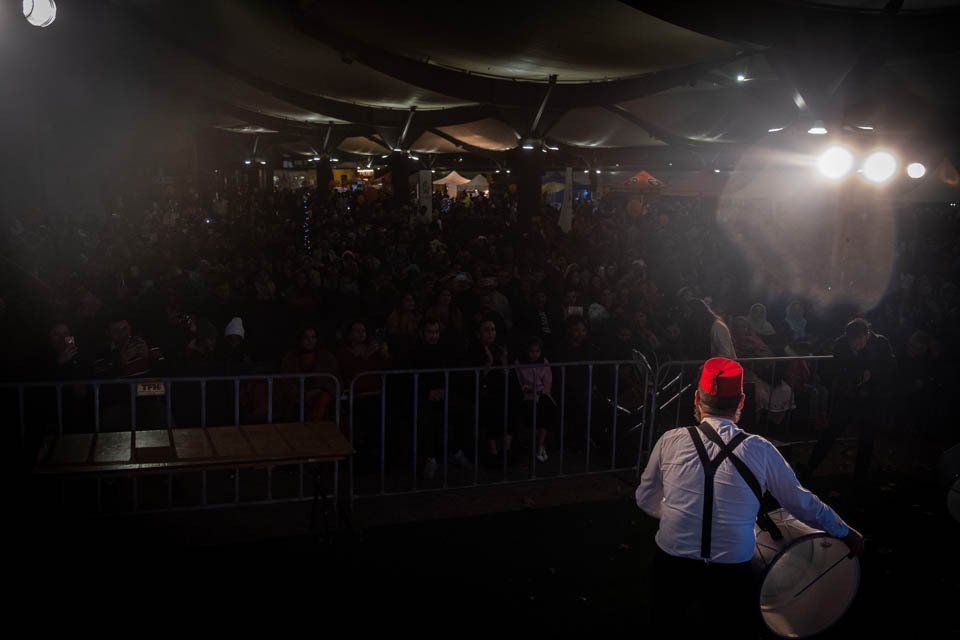 A man is standing on a stage holding a drum in front of a crowd.