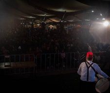 A man is playing a drum on a stage in front of a crowd.