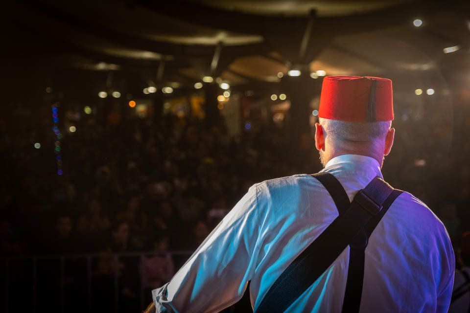 A man wearing a red hat and suspenders is playing a guitar on stage.