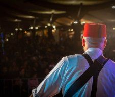 A man wearing a red hat and suspenders is playing a guitar on a stage.