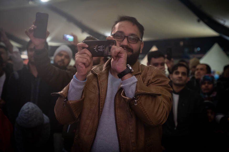 A man is taking a picture of a crowd with his cell phone.