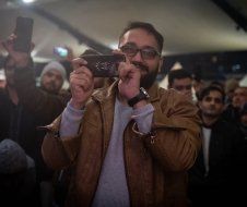 A man is taking a picture of a crowd with his cell phone.