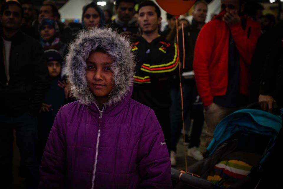 A girl in a purple jacket with a fur hood is standing in a crowd of people.