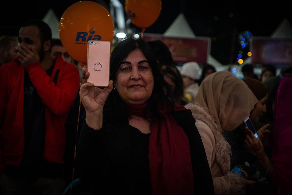 A woman is holding a cell phone in her hand in front of a crowd of people.