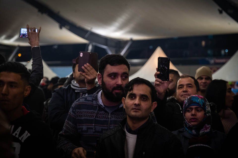 A group of people are standing in a crowd taking pictures with their phones.