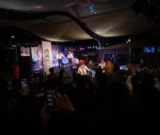 A group of people are standing in a dark room watching a band perform on stage.