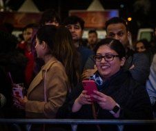 A woman is standing in a crowd of people looking at her cell phone.