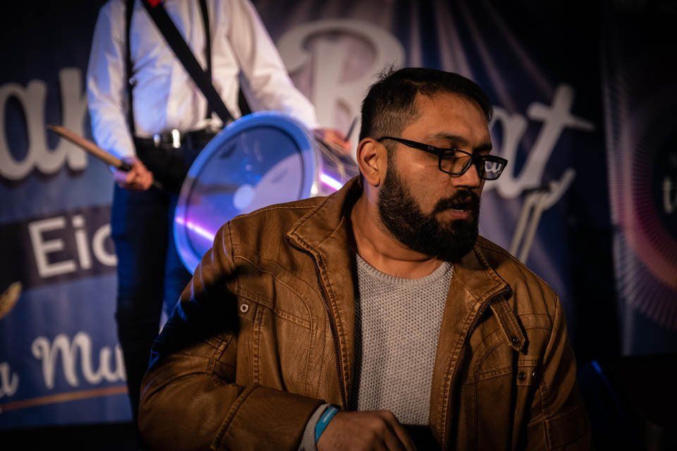 A man with a beard and glasses is playing drums in a band.