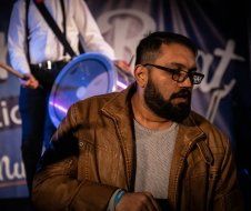 A man with a beard and glasses is sitting in front of a drum set.