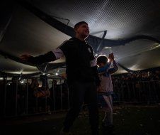 A man and a child are dancing under a tent in the dark.