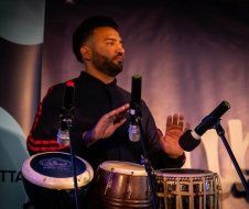 A man is playing drums and singing into a microphone on a stage.