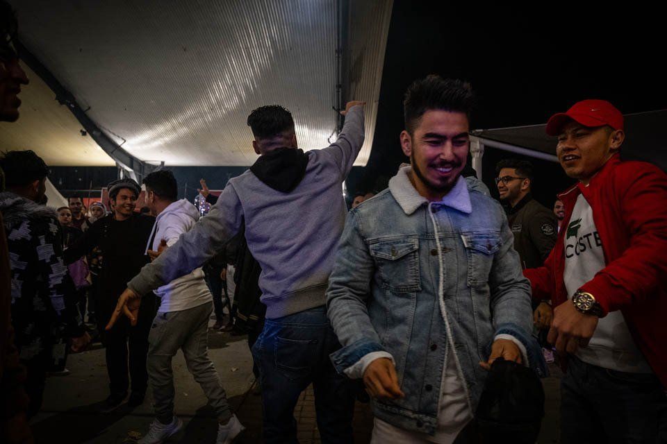 A man in a denim jacket is dancing in a crowd of people.