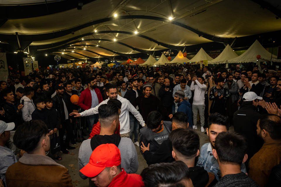 A large group of people are dancing in a tent at a party.