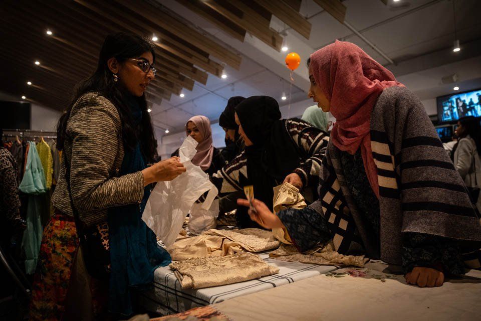 A group of women are standing around a table looking at clothes.