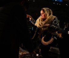 A woman is sitting in a dark room holding a necklace.