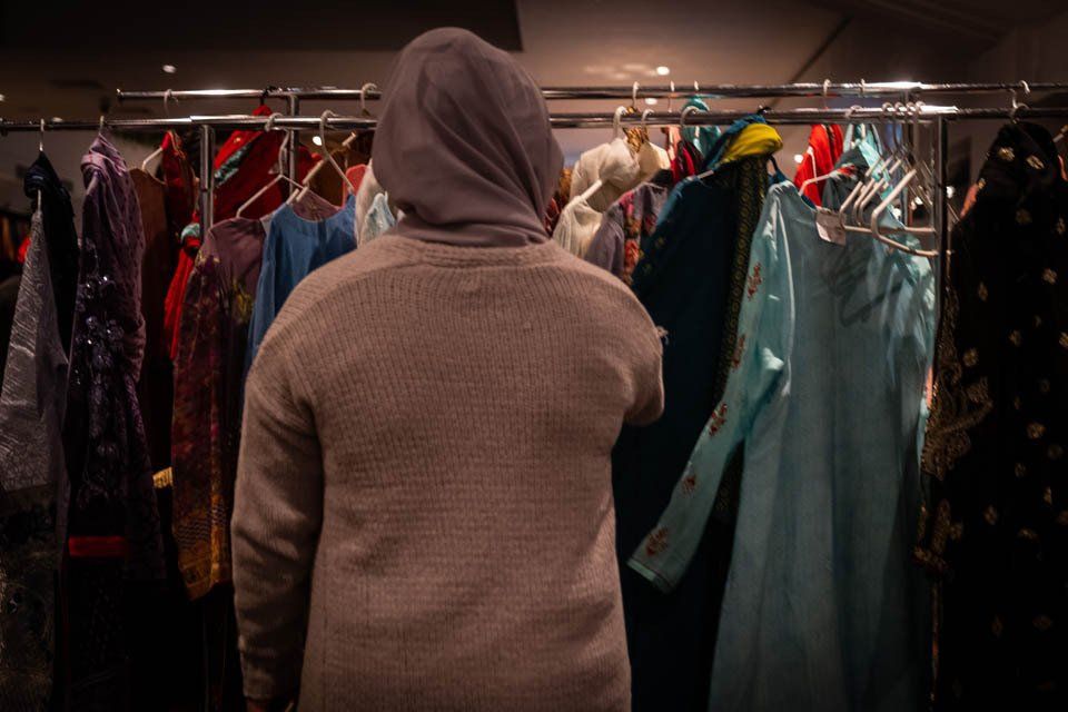 A person in a hoodie is standing in front of a rack of clothes.