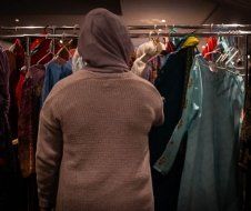 A man in a hoodie is standing in front of a rack of clothes.