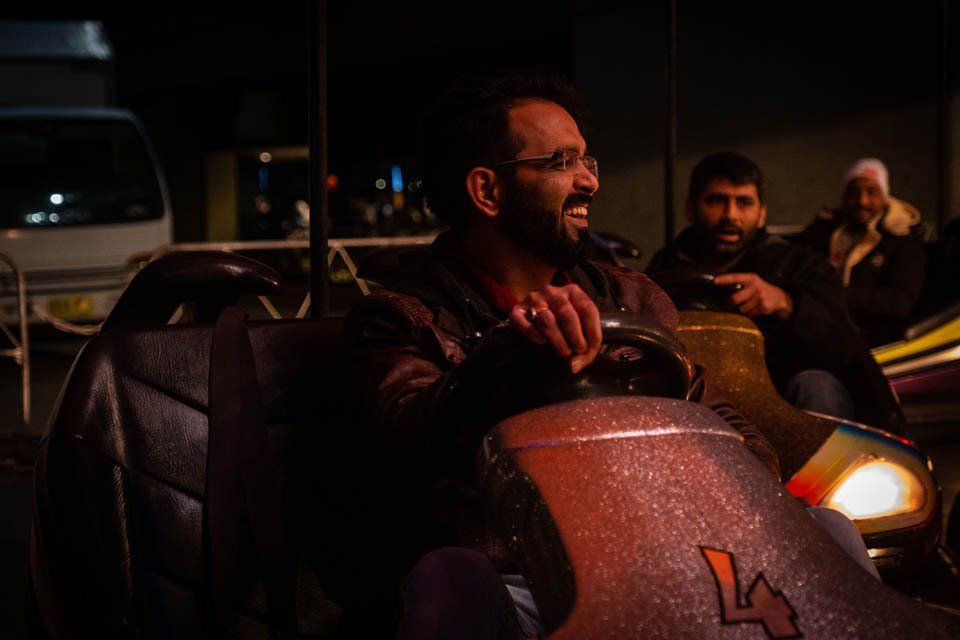 A man is riding a bumper car at a carnival at night.