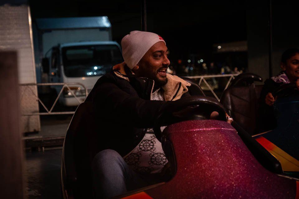A man is riding a bumper car at a carnival at night.