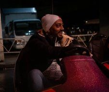 A man is riding a bumper car at a carnival at night.
