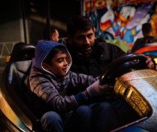 A man and a boy are riding a bumper car at an amusement park.