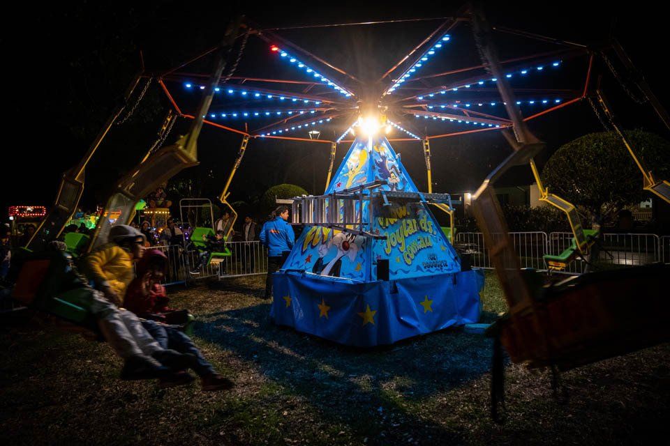 A carnival ride is lit up at night and people are sitting in chairs.
